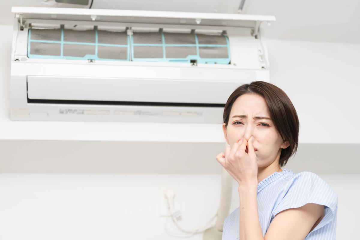 Femme qui se bouche le nez devant un climatiseur
