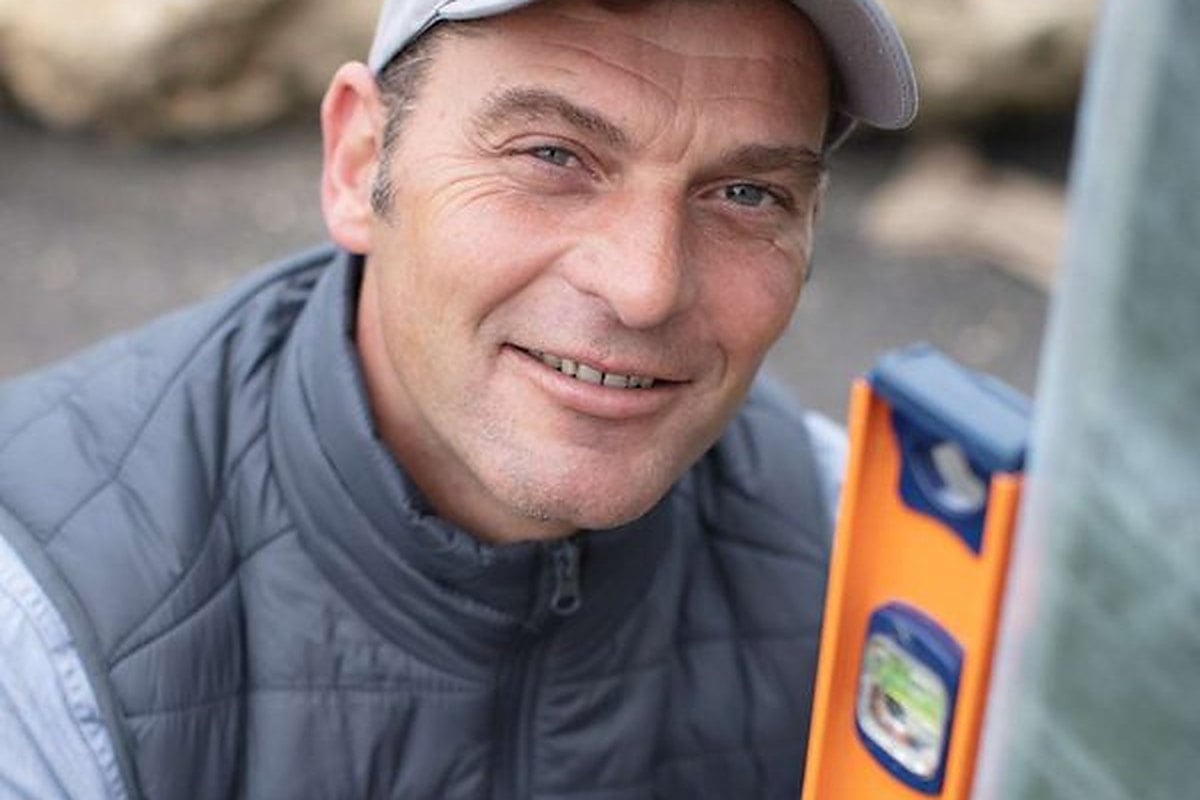 Artisan du bâtiment souriant avec un niveau à bulle sur un chantier de rénovation