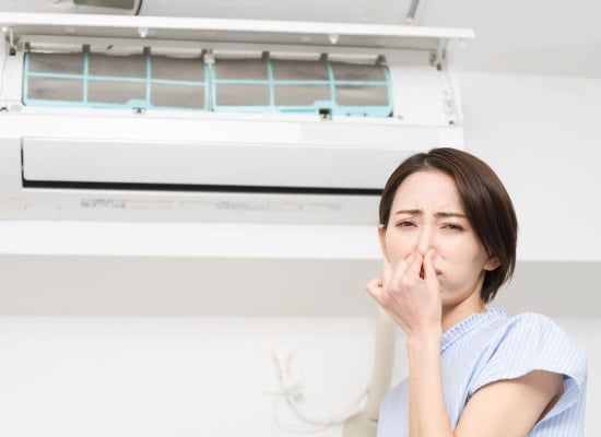 Femme qui se bouche le nez devant un climatiseur
