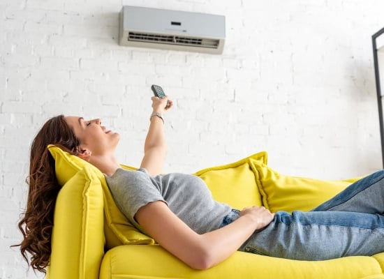 Une femme profitant de la fraîcheur de la climatisation allongée sur un canapé