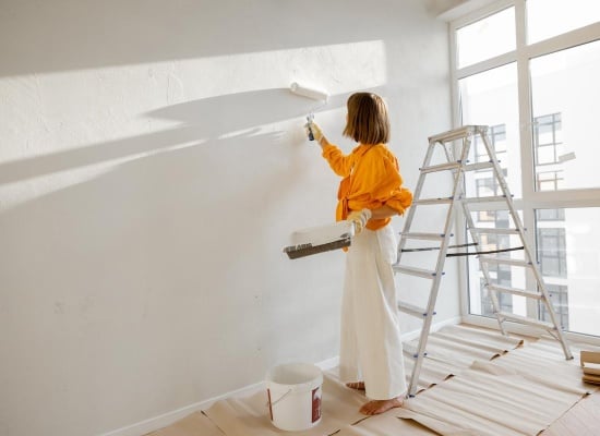 Femme qui peint un mur en blanc avec un rouleau