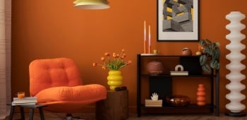 Salon aux murs orange, avec un fauteuil orange, des objets décos aux formes organiques, une lampe en métal et une table d'appoint en bois foncé