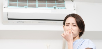 Femme qui se bouche le nez devant un climatiseur