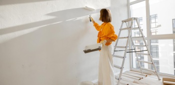 Femme qui peint un mur en blanc avec un rouleau