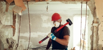 Mur dont une partie est démolie, laissant voir un artisan avec une masse