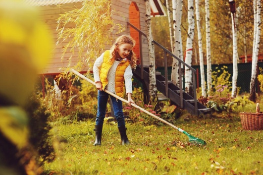 Petite fille ratissant des feuilles d'automne dans le jardin.