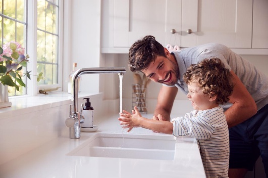 Enfant qui se lave les mains dans l'évier de la cuisine avec son père.
