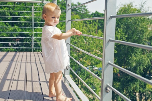 Enfant se tenant au garde-corps d'un balcon non sécurisé.