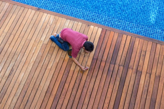 un homme entretien sa terrasse en bois