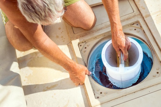 un homme nettoie le filtre de sa piscine