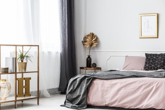 Chambre d'adulte décorée dans un style classique et chic, avec de la literie rose, un plaid gris, et des objets déco dorés.