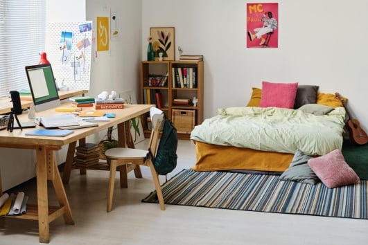 Chambre d'ado avec un lit et un bureau, décorée avec des posters et des coussins colorés.