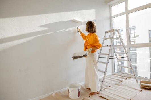 Femme qui peint un mur en blanc avec un rouleau