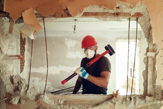 Mur dont une partie est démolie, laissant voir un artisan avec une masse