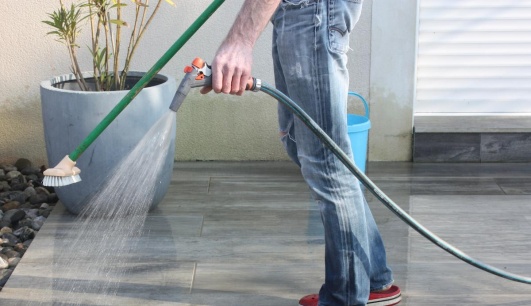 Nettoyage du carrelage extérieur avec un balai et un tuyau d'arrosage