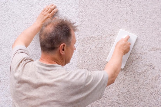 Artisan posant du crépi sur la façade d'une maison