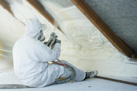 artisan pulvérisant de la mousse en polyuréthane dans les murs d'une maison