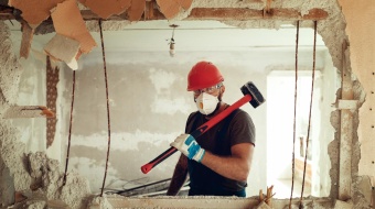 Mur dont une partie est démolie, laissant voir un artisan avec une masse