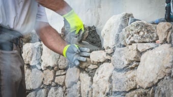 Artisan ajoutant du ciment sur un mur en pierre